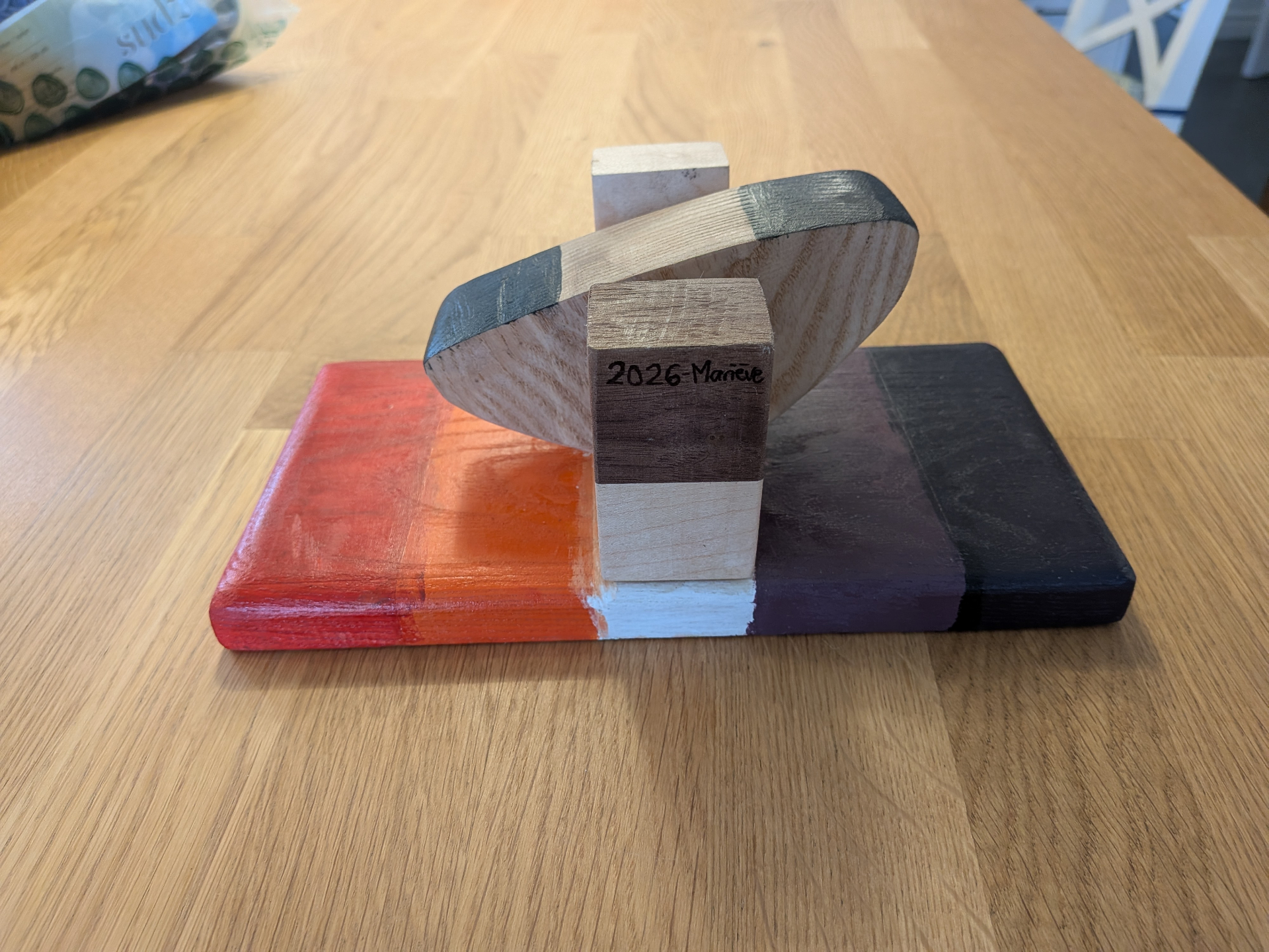 Sculpture en bois Doigts de Fer 2026 Mariève sur planche multicolore